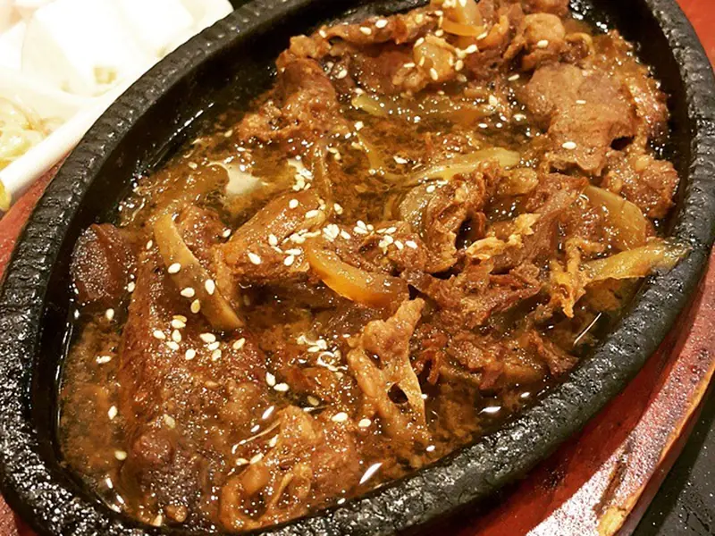 Thin marinated beef cooking on a domed tabletop pan